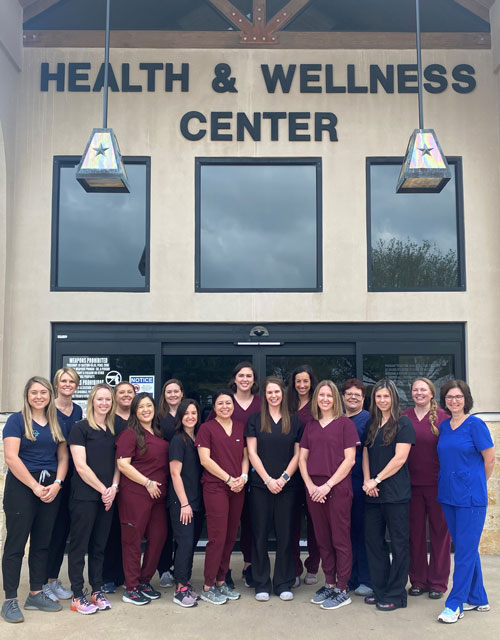 Picture of Therapy Dept staff members wearing scrubs. They are standing in front of the Wellness Center outside.